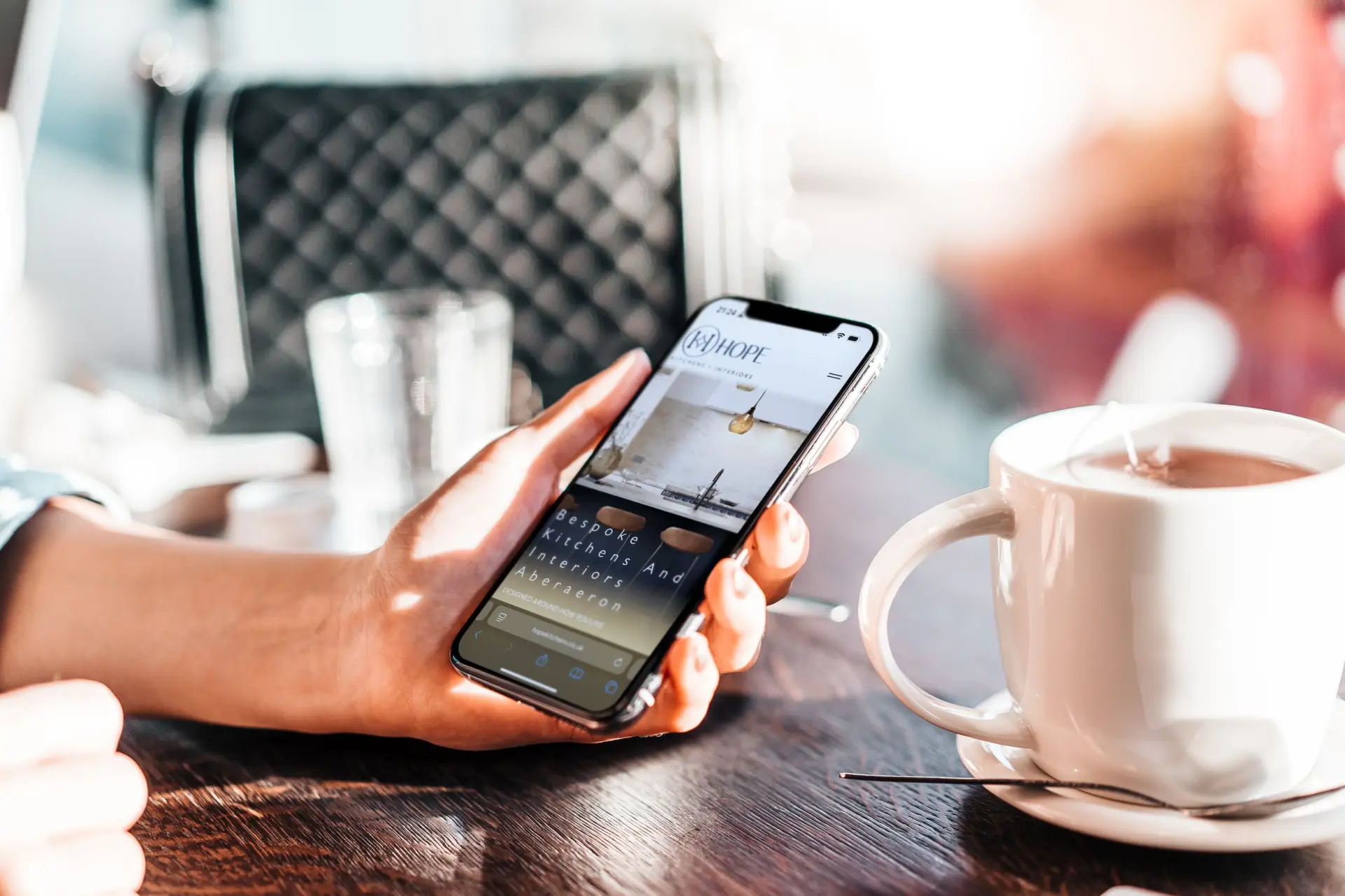 Hand holding a phone showing the Hope Kitchens home page in a café